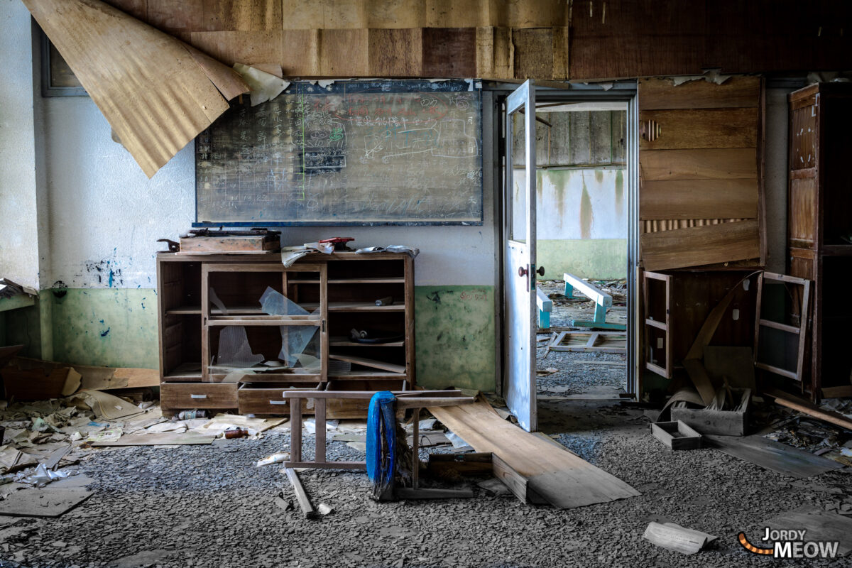 Abandoned teacher’s room on Gunkanjima, Japan, with faded chalkboard and debris-covered floor.
