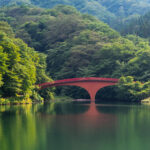 Red arch bridge reflecting on calm forest lake in Gunma, Japan