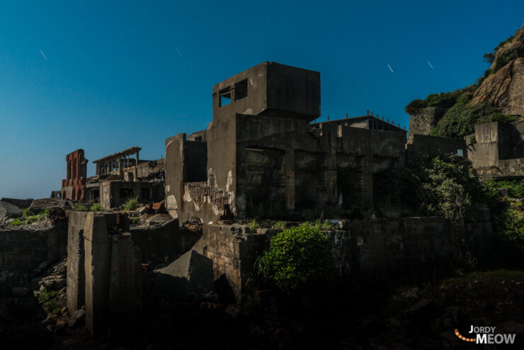 Abandoned coal mining town on Gunkanjima island at night, eerie, decaying industrial buildings.