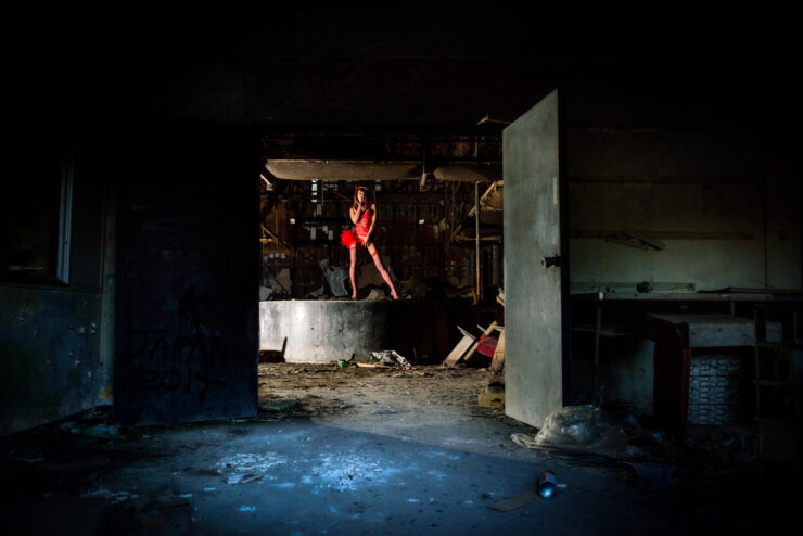 Dynamic dancer in red costume performs gracefully in abandoned space, creating an ethereal atmosphere.