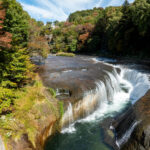 Fukiware Falls in Japan, river rushing through curved rock gorge amid autumn forest.