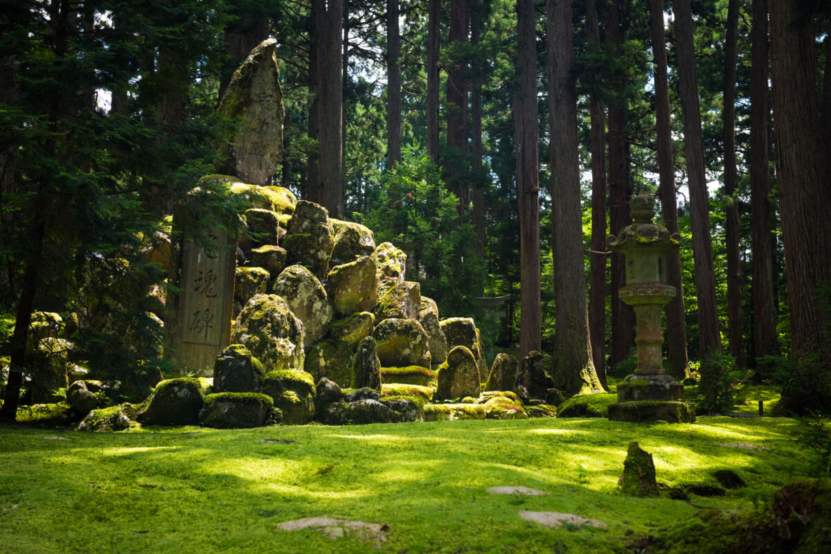 Moss-covered stone ruins, stele, and lantern at Heisenji Hakusan Shrine in cedar forest.