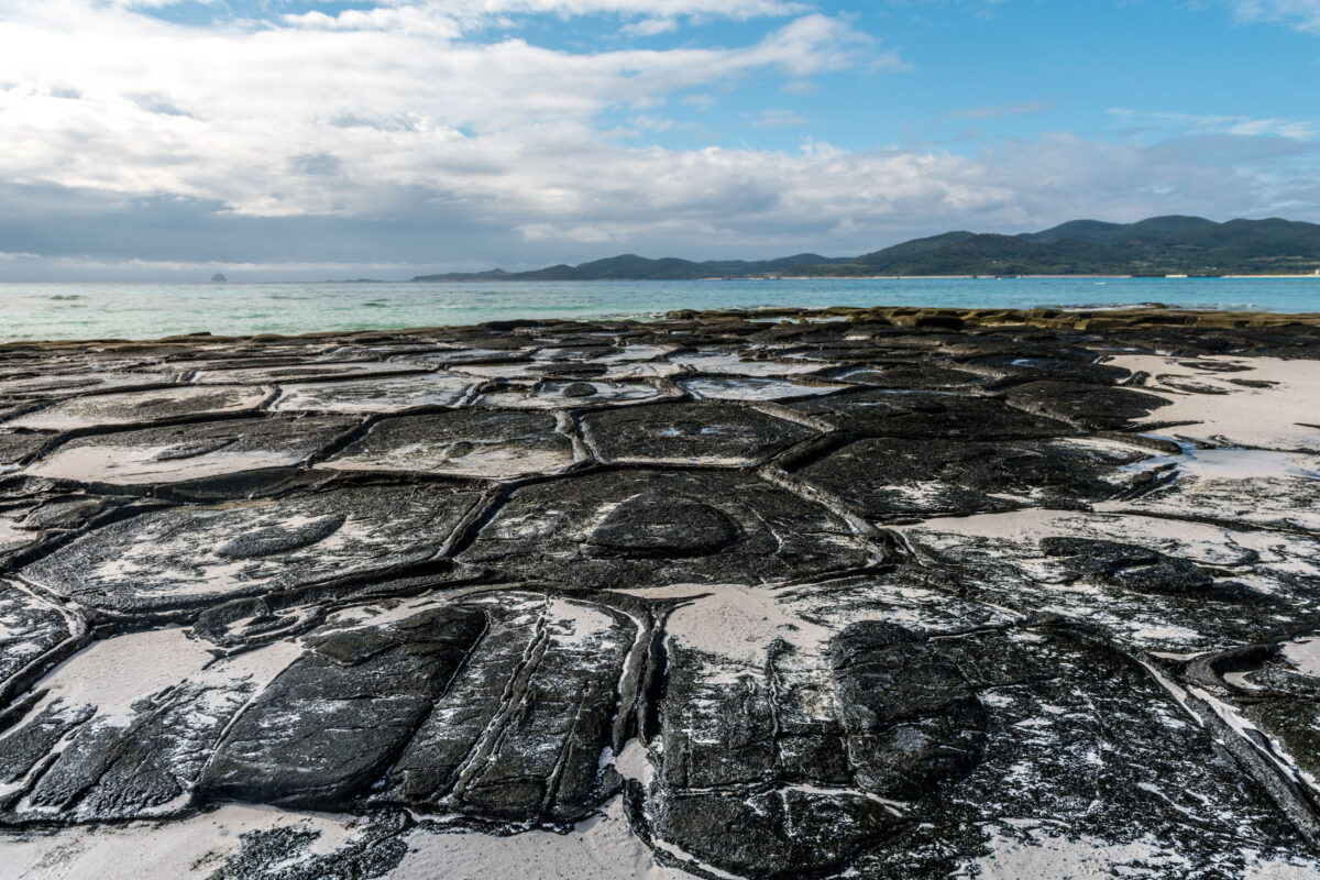Kumejima basalt tide flats leading to turquoise sea and distant green hills