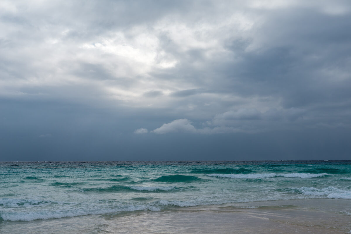 Turquoise waves on Kumejima Island beneath storm clouds along a sandy shoreline