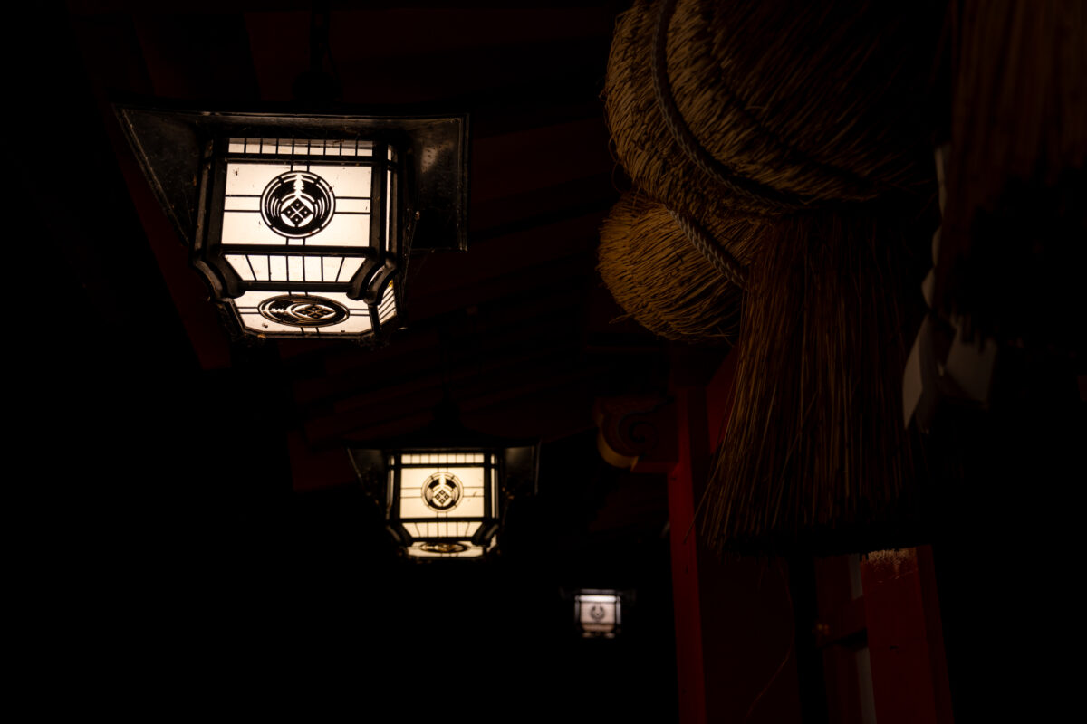 Glowing lanterns line a dark corridor at Taikodani Inari Shrine in Japan at night.