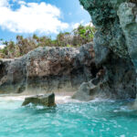 Turquoise cove and rugged limestone cliffs on Miyako Island under a bright blue sky.