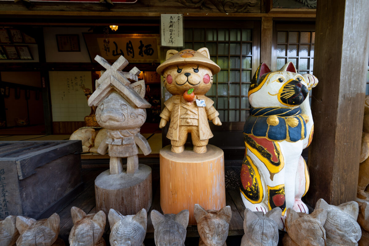 Three whimsical statues, including painted cat, displayed at Unrin-ji temple entrance in Japan.