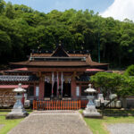 Stone path to Wakaura Tenmangu Shrine in Wakayama, Japan, with lanterns and forest backdrop.