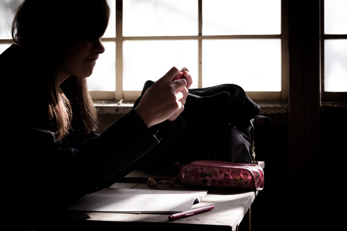 Silhouetted student at desk in abandoned classroom, notebook and pencil case by window light.