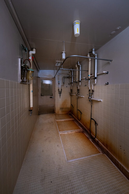 Tiled animal research facility washdown room with exposed pipes, valves, and floor drains