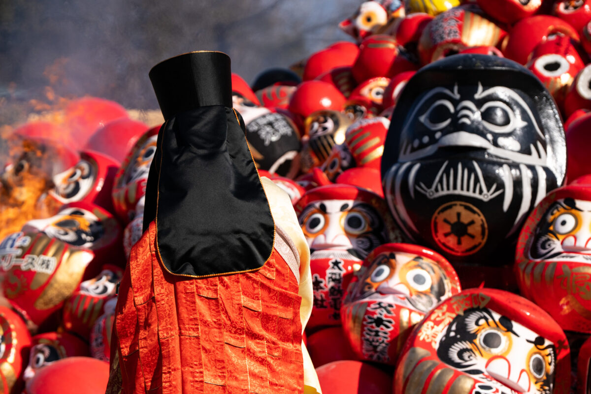 Monk facing pile of Daruma dolls during Shorinzan Temple burning ceremony in Japan.