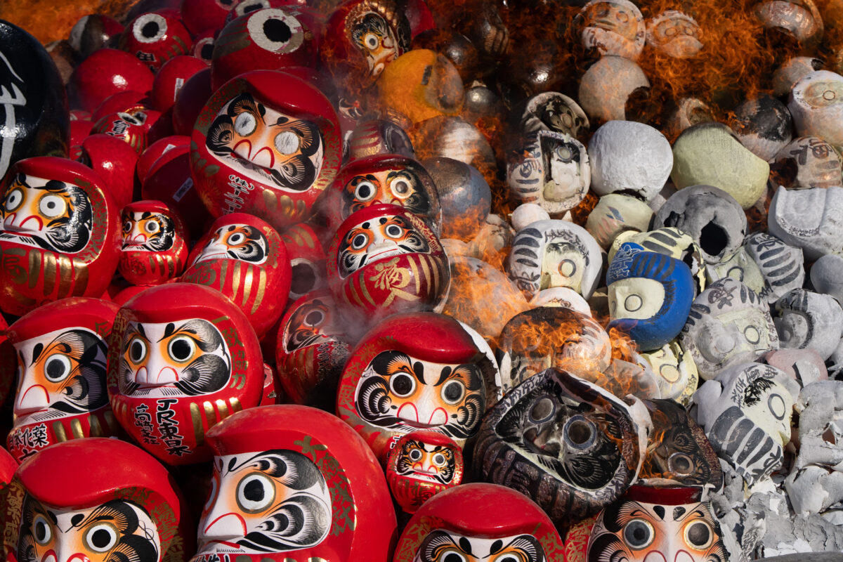 Shorinzan Temple Daruma doll burning ceremony with smoke, flames, and rows of red dolls.