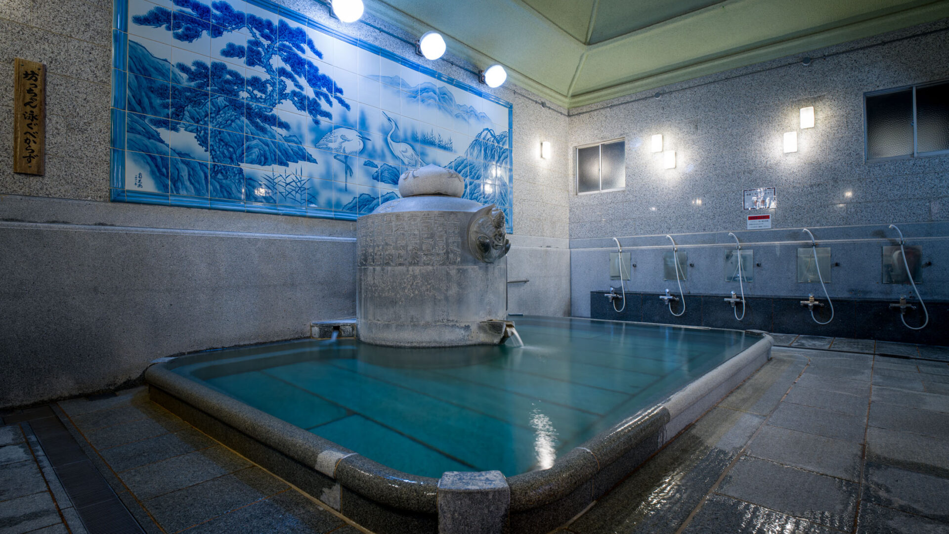 Interior of Dōgo Onsen bathhouse with steaming stone bath, blue mural, and washing stations