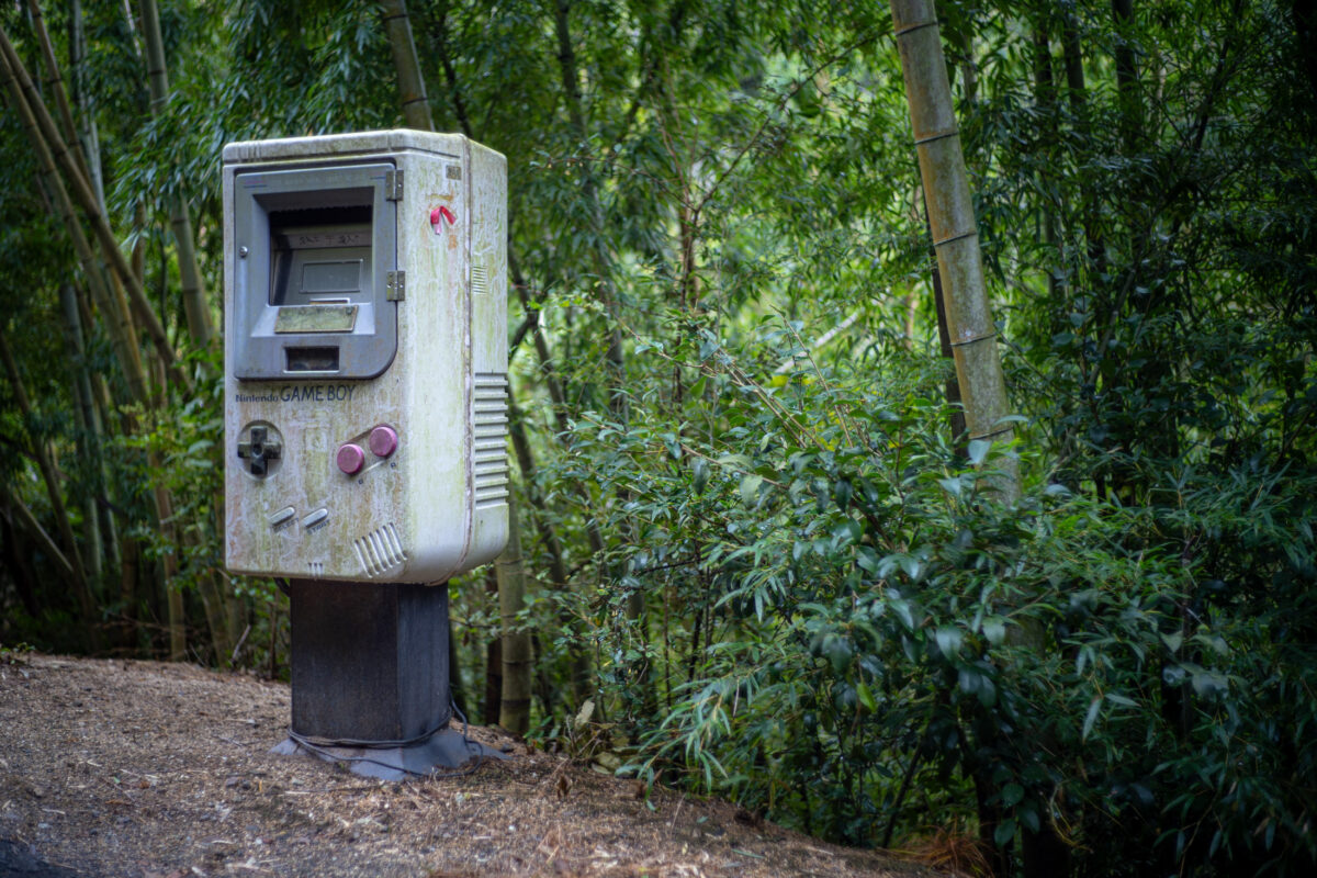 Giant weathered Game Boy-shaped mailbox on a post in a bamboo forest
