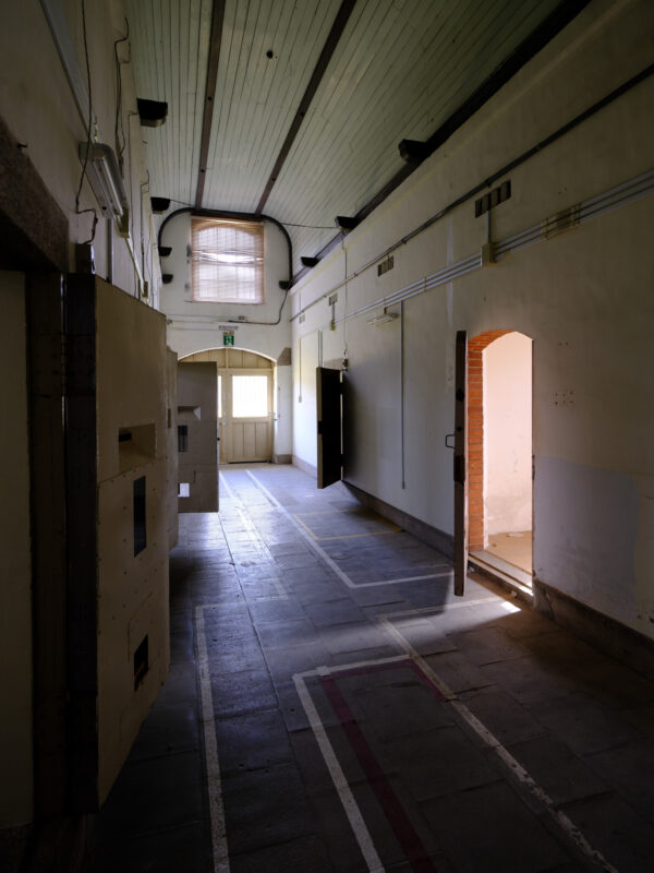 Empty corridor in historic Nara Prison with cell doors, open doorway, arched window light.