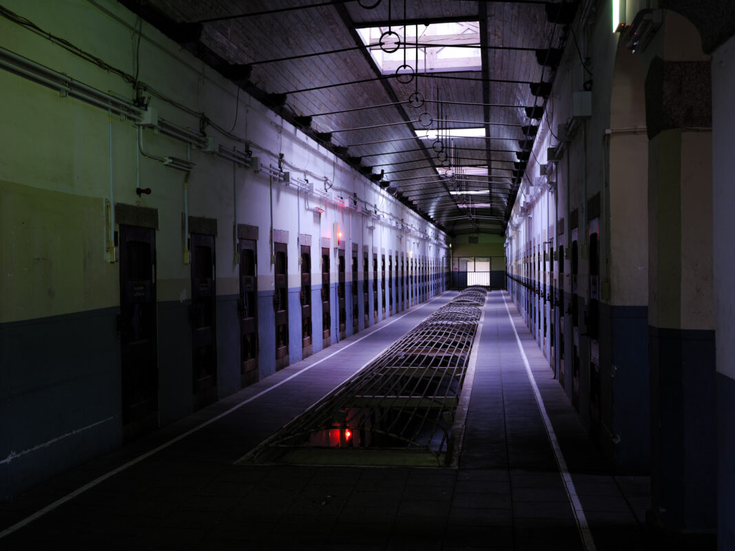 Symmetrical Nara Prison cellblock corridor with metal doors and central floor grate.