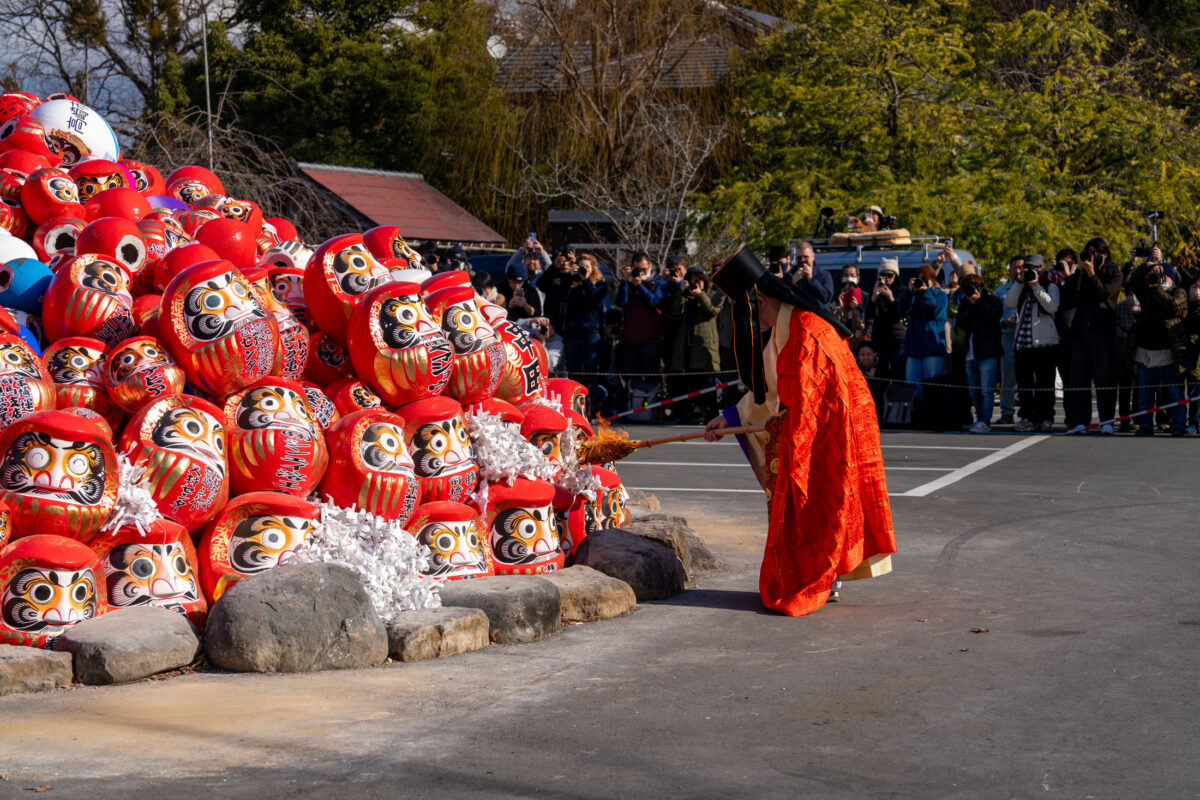 Monk blesses pile of red Daruma dolls at Shorinzan Temple ceremony in Japan.