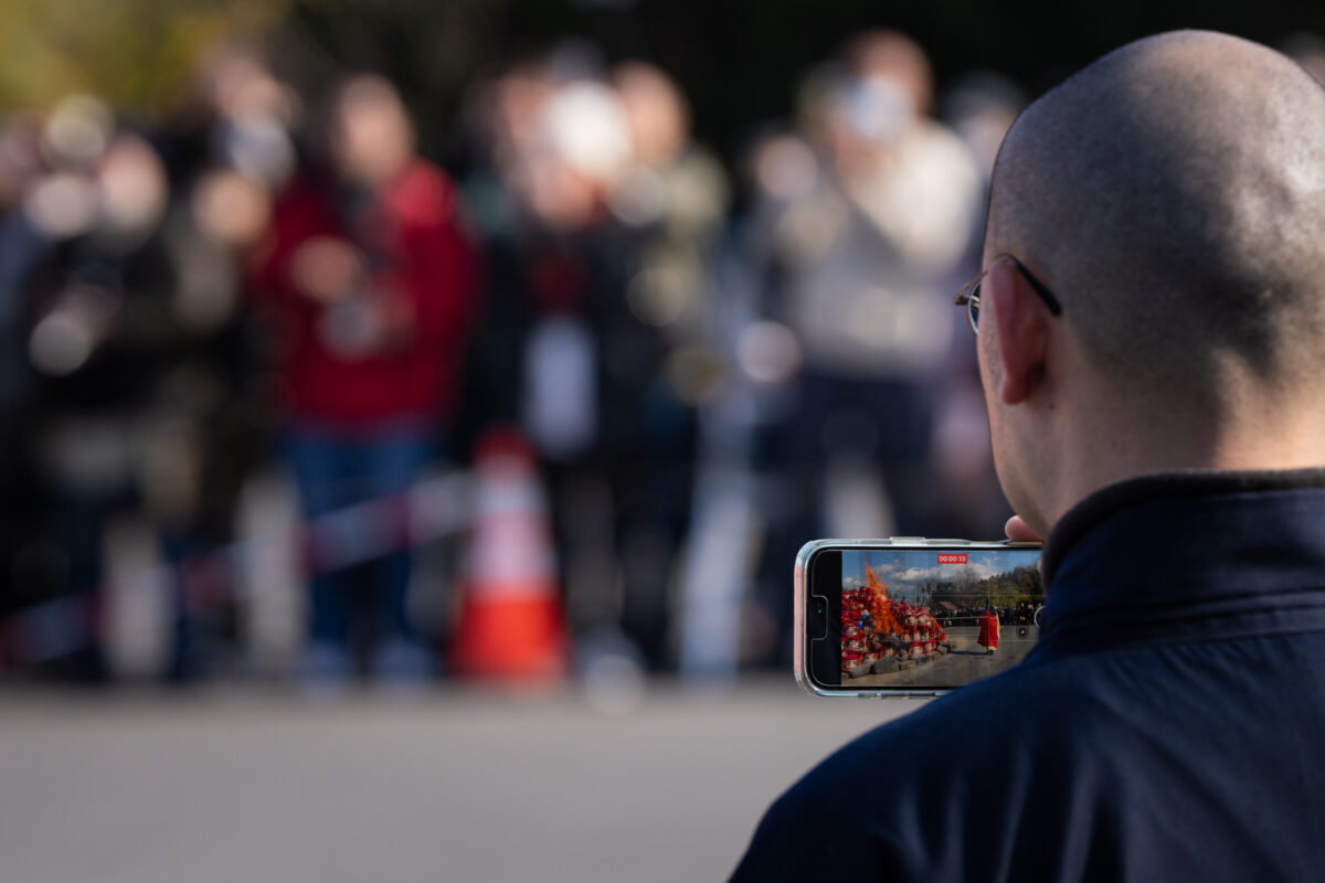 Visitor photographs Shorinzan Temple Daruma Festival on smartphone, red Daruma dolls on screen.