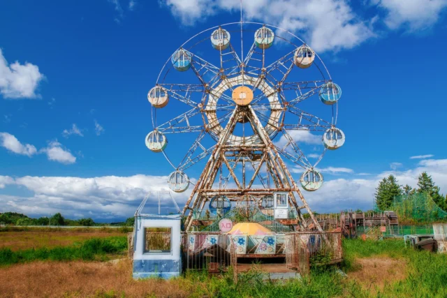 Wheels rust in stillness, Blue skies dance with clouds above, Nature takes the stage.---静けさに錆びた車輪、 雲と踊る青空、 自然が舞台を奪う。---#offbeatjapan #japan #abandonedplaces #ferriswheel #naturetakesover #melancholicbeauty #ruraljapan